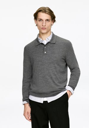 Gray knit polo sweater with a collar, featuring two buttons, layered over a white and blue striped shirt, worn with dark trousers.