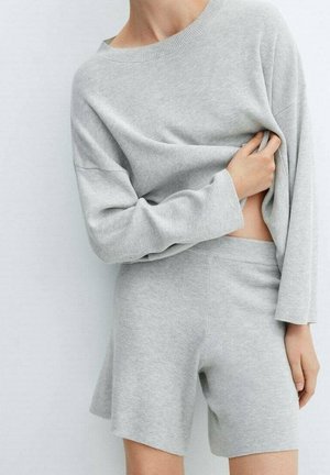 Persoon draagt een lichtgrijs geribd gebreid topje met lange mouwen en bijpassende shorts met hoge taille, die gedeeltelijk wordt opgetild om de taille te tonen.