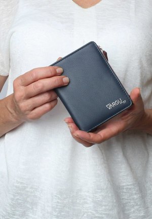 Navy blue leather wallet featuring a textured surface, zip closure, and silver logo detail. Compact, rectangular shape held in hands.