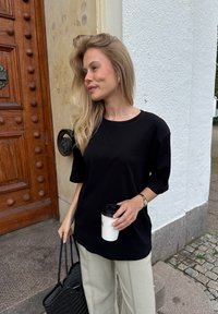 Juodas per didelis marškinėliai su trumpomis rankovėmis, derinami su šviesiai smėlio spalvos plačiomis kelnėmis. Laikoma balta kavos puodelis, nešama juoda nertinė rankinė.