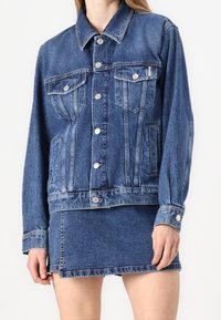 Jeansjacka, ljusblå, med två bröstfickor, silverknappar och en avslappnad passform. Matchas med en matchande jeansminikjol.