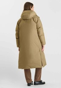 Olijfgroene lange gewatteerde jas met een capuchon, met een gladde textuur en zijsplitten. Draag met bruine gestructureerde broek en zwarte schoenen.