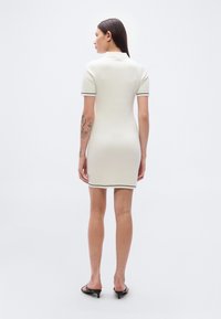 Πλεκτό φόρεμα πόλο σε εκρού χρώμα με κοντά μανίκια, ριμπ κολάρο, τονικό διακοσμητικό περίγραμμα και εφαρμοστή γραμμή. Λείο υφή με μοτίβο διαμαντιού.