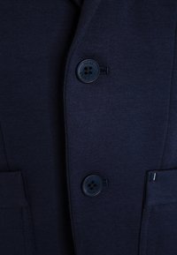 Námořnický blazer s dvěma černými knoflíky, texturovanou tkaninou a kapsou s jemným akcentem na předním švu.