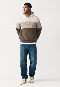 Kapucar v bež in rjavih barvnih blokih, iz mehkega blaga. Kombiniran z modrimi kavbojkami in belimi supergami z rjavimi poudarki.