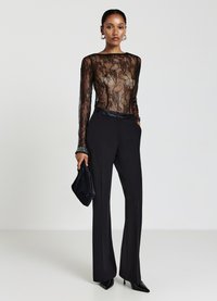 Schwarzer Spitzen-Bodysuit mit langen Ärmeln, der mit floralem Muster und Rundhalsausschnitt gestaltet ist. Kombiniert mit hoch taillierten schwarzen Hosen und Stöckelschuhen.