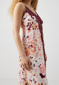 Kwiatowa sukienka w białym kolorze z różowymi i pomarańczowymi wzorami, z bordową koronką wzdłuż dekoltu oraz cienkimi ramiączkami.