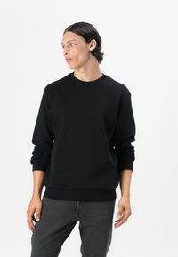 Svart crewneck sweatshirts i ett mjukt tyg, med ribbade muddar och fåll. Modellen har på sig mörkgrå jeans. Enkelt mönster, utan mönster eller detaljer.