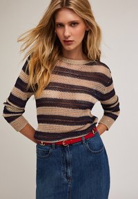 Gestreifter Strickpullover in Beige, Marineblau und Braun mit lockerer Passform und dreiviertel Ärmeln, kombiniert mit einem roten Gürtel und einem Jeansrock.