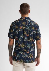 Camicia a maniche corte con sfondo navy e una vivace stampa di palme e chitarre, realizzata in tessuto leggero per garantire comfort.
