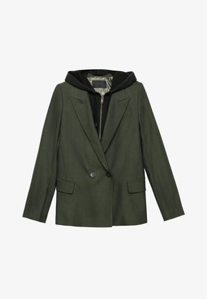 Blazer verde su misura con spalle strutturate, due tasche frontali e un felpa nera indossata sotto. Texture liscia con chiusura a bottone.