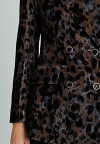 Blazer in stampa leopardata marrone e nera, texture in velluto, design doppiopetto, bottoni circolari argentati e due tasche laterali.