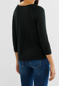 Svart långärmad topp med bred rund halsringning, slät yta och avslappnad passform, tillsammans med blå denimjeans med klassisk skärning och minimal slitning.