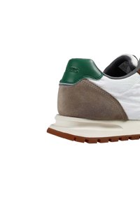 Zapatilla blanca con contrafuerte en el talón de cuero verde, detalles en ante gris y una entresuela texturizada. Suela exterior de goma con un patrón de tracción robusto.