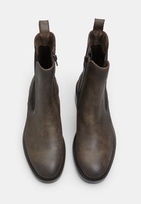 Botas de tobillo de cuero marrón con una textura suave, cierre de cremallera lateral y lengüeta. Punta redonda y detalle de costura en contraste.
