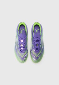 Paarse en groene voetbalschoenen met een reliëfontwerp, met gebogen lijnen en veters, en "FS" en "80" gedrukt op de zijkanten.