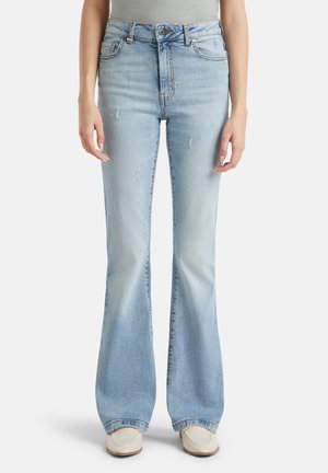 Jeans acampanados de un azul claro con una cintura alta, que presentan zonas desgastadas y pequeños detalles deshilachados. Diseño clásico de cinco bolsillos y herrajes plateados.