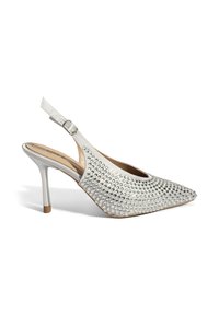 Zilveren slingback pump met puntige neus, versierd met zilveren studs. Voorzien van een naaldhak en een lederachtige afwerking.