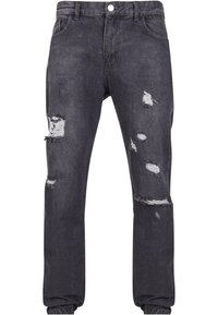 Vaqueros de mezclilla gris oscuro con múltiples agujeros desgastados y bordes deshilachados; diseño clásico de cinco bolsillos con cierre de botón y pasadores para cinturón.
