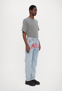 Tricou oversized gri, blugi deschiși cu grafică roșie de pisică și pantofi negri slip-on. Design simplu cu o croială casuală și accente proeminente.