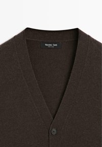 Cardigan marron foncé à col en V avec un seul bouton noir, présentant une étiquette Massimo Dutti cousue à l'intérieur du col.