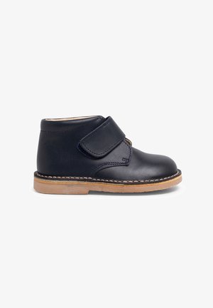 Stivale alla caviglia in pelle blu navy con strap in velcro, suola in gomma beige, punta rotonda e cuciture visibili sui bordi.