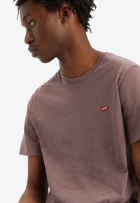 Kurzärmliges Crewneck-T-Shirt aus gedämpftem Mauve-Baumwolle. Hat ein kleines rotes Levi's-Logo auf der linken Brust und eine einfache, entspannte Passform.