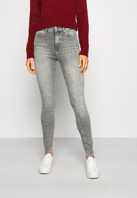 Jeans skinny grises de mezclilla, con un diseño clásico de cinco bolsillos, sutil desvanecimiento y una cintura de altura media. Combinados con zapatillas blancas.