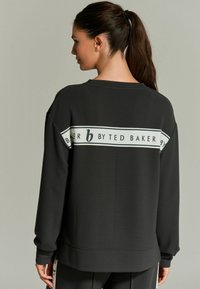 Czarny sweatshirt z żeberkowym wykończeniem, w oversize'owym kroju, z białym pasem z napisem "b by Ted Baker" na plecach.