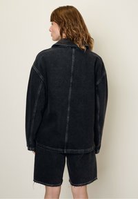 Zwarte denim jack met een oversized pasvorm en zichtbare stiksels, gecombineerd met bijpassende zwarte denim shorts met een rafelige zoom.