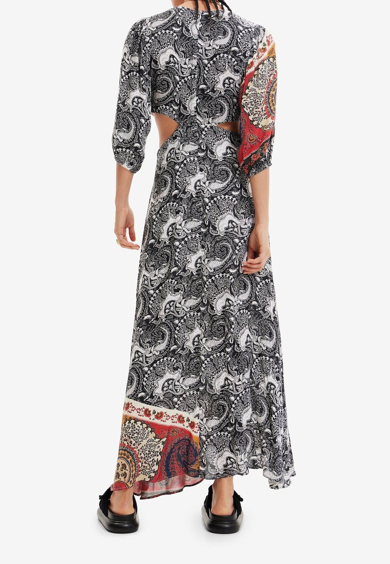 Femme portant une longue robe à motifs avec des découpes à la taille et des manches et un ourlet colorés en contraste, associée à des chaussures noires sans lacets.