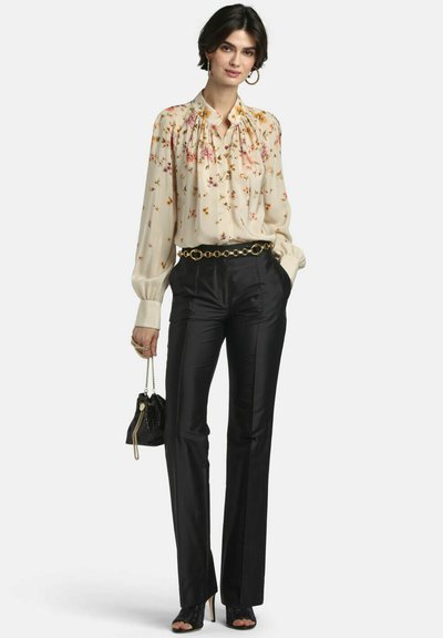 Woman wearing a floral long-sleeve blouse tucked into black high-waisted pants with a gold chain belt, holding a black handbag with a chain strap.