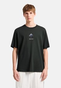 Camiseta negra de algodón con un logotipo metálico en forma de diamante en el pecho y mangas cortas. Diseño clásico de cuello redondo.