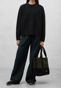 Pull noir en maille avec un ourlet côtelé, accompagné d'un pantalon ample vert foncé et d'un sac cabas vert et noir. Chaussures noires avec semelle texturée.