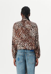 Leopardenmuster Bluse mit langen, puffigen Ärmeln, leichtem Stoff und Kragen, kombiniert mit hoch taillierten Jeans mit bestickten Akzenten.