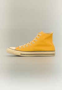 Υψηλού άνω sneaker σε έντονο κίτρινο καμβά με λευκές τρύπες για κορδόνια, κρέμ λαστιχένια μύτη και μαύρη ρίγα κατά μήκος της σόλας.