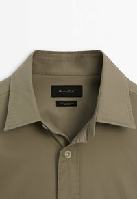 Collet et partie supérieure avant d'une chemise beige en coton-élastane à boutons, avec étiquette de marque "Massimo Dutti" à l'intérieur du col.