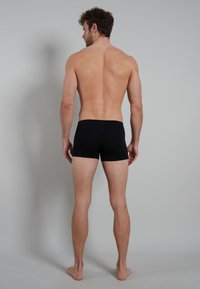 Boxer shorts en tissu noir, avec un ajustement serré et sans motifs ni éléments visibles, vus de l'arrière sur un modèle à la peau nue.