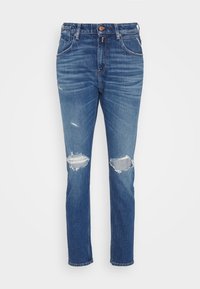 Siniset farkut suoran lahkeen kanssa, kevyellä kulutuksella ja kahdella revityllä polvipatchilla. Varustettu nappikiinnityksellä ja viisi taskua sisältävällä suunnittelulla.