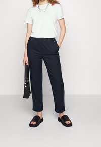 Svarta, löst sittande byxor med elastisk midja, sidofickor och uppvikta nederkanter, kombinerat med en vit t-shirt och svarta slidesandaler.