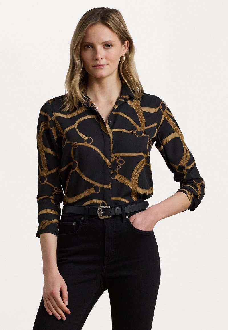 Camicia nera con bottoni e motivo a catena dorata, realizzata in tessuto liscio. Presenta maniche lunghe e un colletto. Abbinata a jeans neri e una cintura.