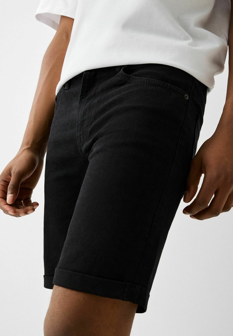 Černé džínsové šortky s ohrnutými lemy, s pěti kapsami a jemným prošíváním. Pas obsahuje detail s kovovým knoflíkem.