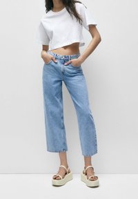 Lichtblauwe wijdgebrepte jeans met een hoge taille, een vervaagde denim textuur en gestikte accenten, gecombineerd met een cropped wit t-shirt en platform sandalen.