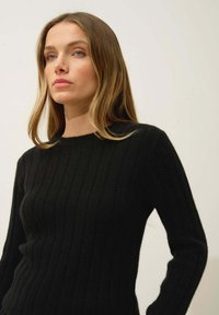 Pull en tricot noir côtelé avec un décolleté rond et des manches longues, doté d'une texture douce et d'une silhouette ajustée.