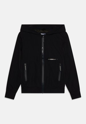 Juodas užtrauktuku užsegamas džemperis su pamuštu kapišonu, dviem užtrauktukais užsegamais kišenėmis, elastingomis rankogaliais ir apatinėmis briaunomis, su subtiliu logotipo akcentu.