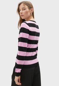 Maglione a righe nere e rosa con scollo rotondo, polsini aderenti e orlo a coste. Il tessuto appare morbido e con una texture liscia.
