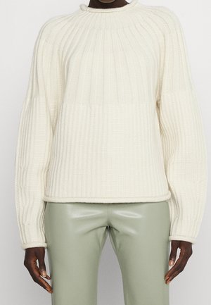 Cremefarvet strikket sweater med ribbet tekstur, oversized ærmer og høj krave. Sammen med lysegrønne faux læderbukser.