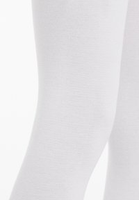 Białe legginsy wykonane z gładkiego, elastycznego materiału. Zbliżenie pokazuje równą teksturę i dopasowany krój bez wzorów czy akcentów.
