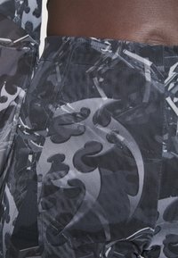 Tissu noir et gris avec des motifs abstraits et des textures, présentant une vue rapprochée des coutures et d'un matériau extensible.