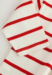 Manica di camicia in cotone a righe rosse e bianche, con una texture morbida, orlo dritto e dettagli di cucitura visibili.
